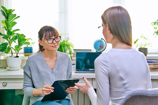 Young female at therapy meeting with psychotherapist. Session of teenage student girl, psychologist with clipboard talking to patient. Psychology, psychotherapy, treatment, youth mental health