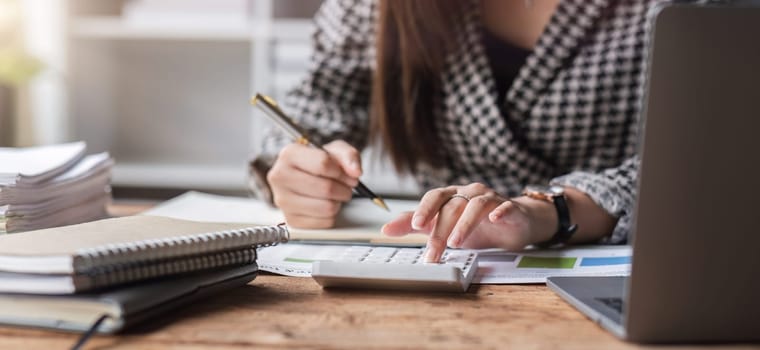 Close up, Business woman using calculator for do math finance on wooden desk in office and business working background, tax, accounting, statistics and analytic research concept..