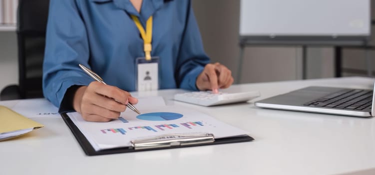 Close up Business woman using calculator and laptop for do math finance on wooden desk in office and business working background, tax, accounting, statistics and analytic research concept.