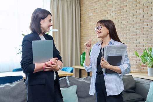 Two businesswomen talking and discussing in office. Female colleagues, manager and employee analyze and discuss documents, contracts, financial reports. Work law finance teamwork people job concept