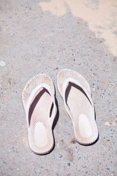 Closeup of pair of old and used white rubber sandals on concrete surface on hot sunny summer day