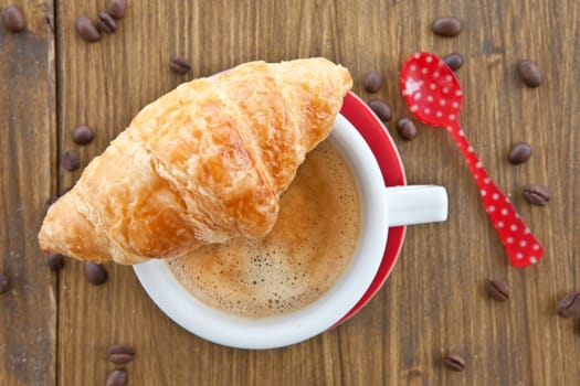 Red cup with coffee and fresh croissant