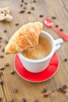 Red cup with coffee and fresh croissant