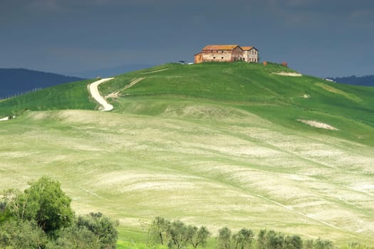Tuscan  landscape with farmhouse  on the hill. Storm dark sky in the background. .
