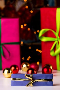 Christmas bulbs and gifts wrapped in magenta and crimson in soft focus enhancing the sharp outlines of the blue box and golden bow in front..