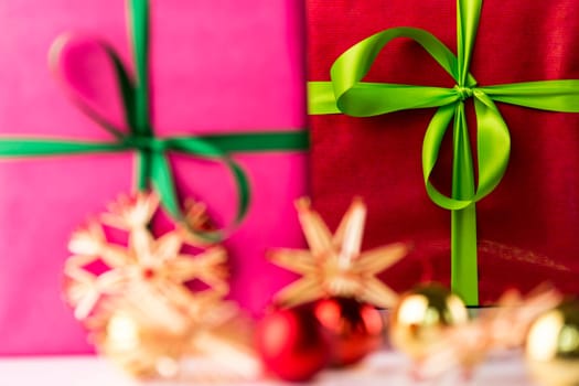 An emerald ribbon and crimson box in the background contrasting with the soft shapes of a magenta gift, straw stars and baubles in the front..