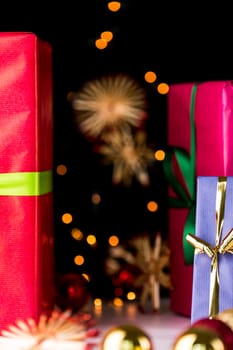 Crimson and blue gift boxes in focus in the mid-ground are giving way to the soft forms of festive spheres, straw stars and twinkles..