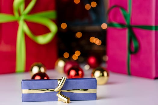 Festive presents wrapped in magenta, red and blue. The golden bowknot is in focus and does correspond with the twinkles of the glitter balls in the rear..