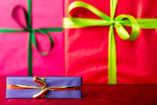 Two big presents wrapped in crimson and magenta. Their indistinct outlines do contrast with the sharp contours of the small blue gift and golden bow in front..