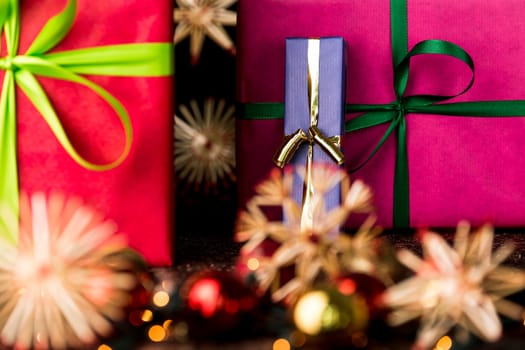 The sharp contours of emerald and golden bowknots tied around a blue and magenta gift box do contrast with the soft shapes of Christmas glitter balls and straw stars..