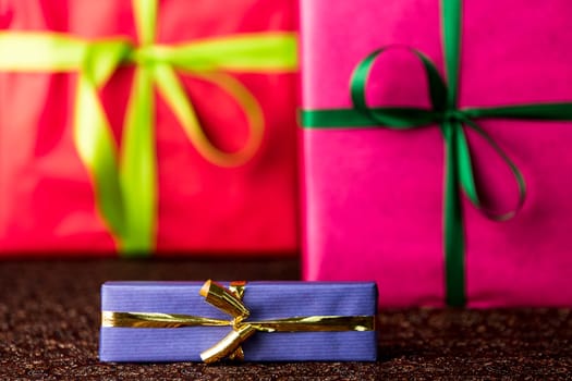 The golden bow and blue wrapping of a small gift box are in focus and do contrast with the red and magenta color-fields of two larger presents..