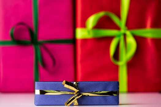Magenta and red color-fields of box surfaces in contrast with the shape of green bows. Their soft focus is augmenting the sharp outlines of the golden bowknot and blue wrapping in front..
