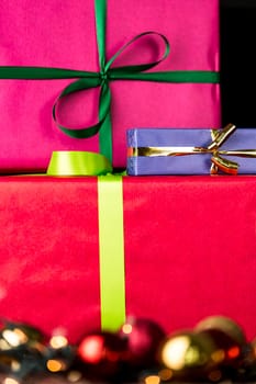 The edgy, flat surfaces of three gifts wrapped in vibrant colors contrasting with the blurry specular highlights of glitter balls in soft focus..