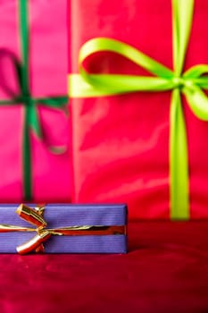 The sharp contours of a blue present tied with a golden ribbon placed against the backdrop of purple cloth and two gifts wrapped in magenta and red..