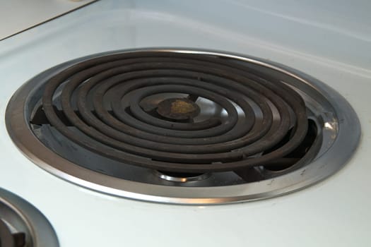 A coiled electric heating element on a modern stove, rusted with chrome ring on white stove top.