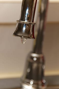 A chrome kitchen water faucet up close with water drop drip.