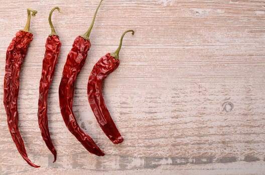 Four dried chilies on a rustic wooden background with space for text