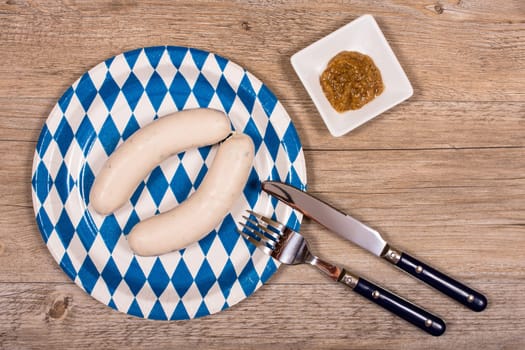 Plate with cutlery and white sausage and mustard on a wooden table