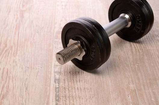 Fitness background with a dumbbell on a wooden floor with space for text