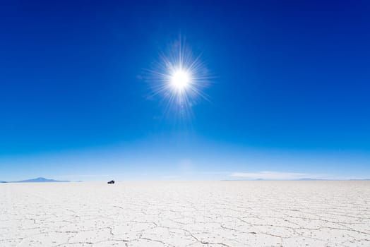 View of the sun over the Uyuni Salt Flats in Bolivia with an SUV in the background.