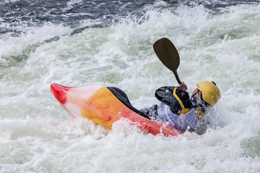 an active male kayaker rolling and surfing in rough water