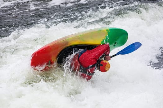 an active male kayaker rolling and surfing in rough water