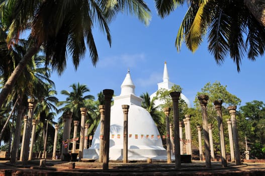 Circle of ancient pillars and white washed Ambasthala stupa, overtowered by hilltop Mahaseya Dagoba, Sri Lanka at Mihintale, Sri Lanka