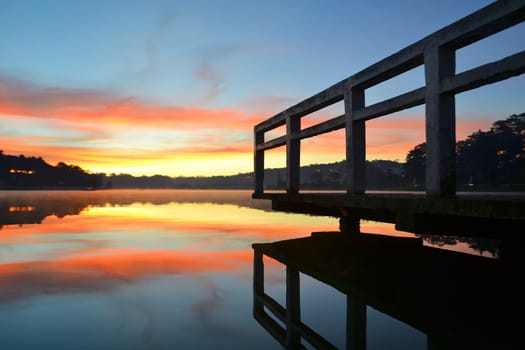 wooden pier on lake in summer morning, the lake being perfectly quiet and reflecting sun and pier
