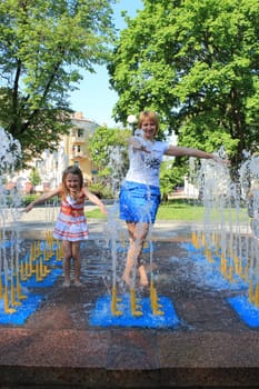 Mother and her daughter playing in the city fountain in the spring