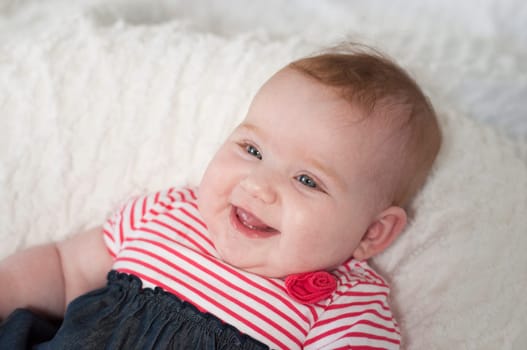 Happy laughing beautiful newborn baby in a colorful red and white striped top lying on its back smiling happily