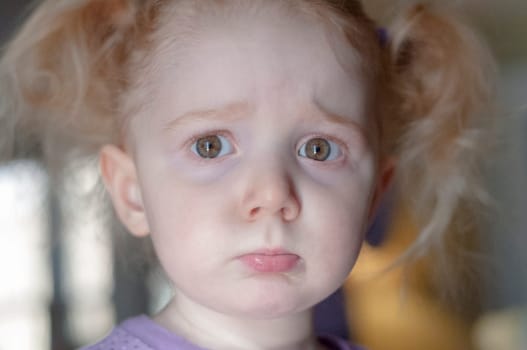 Close up portrait of a cute little redhead girl with a sad pouting expression and big sulky eyes looking straignt at the camera