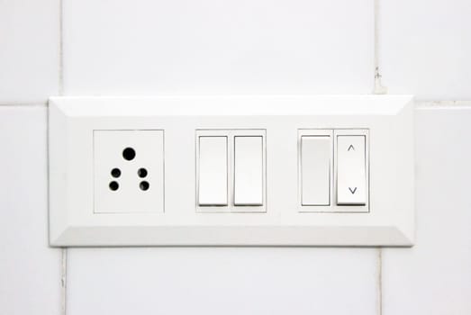 White electrical switch panel and plug point on white tiled wall