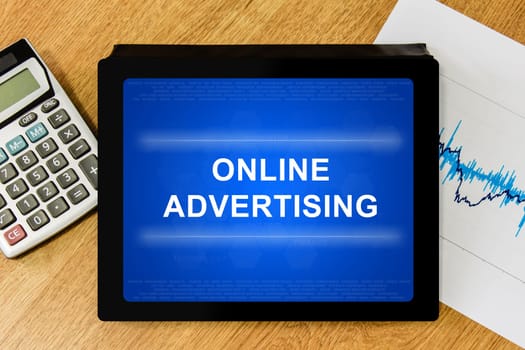 online advertising word on digital tablet with calculator and financial graph
