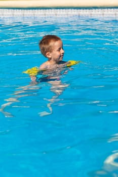 Happy boy swimming with floaties in swimming pool