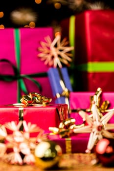 Six Christmas presents in monochrome gift-wrapping. Focus is set on the golden bow around the small crimson red gift on the left. Baubles and stars are outside the shallow depth of field..