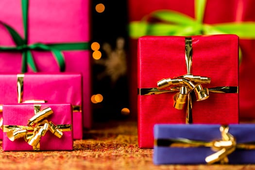 Christmas presents in plain colors placed on a festive cloth. Seasonal background with plenty of text space. Shallow depth of field. Crimson box in focus..