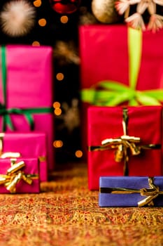 Plain presents with bows placed on a warm-colored, cloth. Plenty of text space. Christmas glitter balls and stars blurred. Seasonal background with shallow depth of field. Focus on blue box..