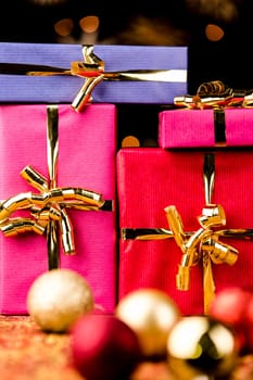 Close-up shot of presents wrapped with golden bows. Tightly framed. Shallow depth of field. Blurred baubles in the front. Background for Christmas and other festive occasions..
