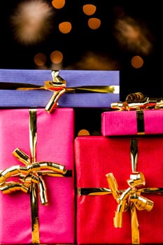 Tightly framed shot of four wrapped presents with golden ribbons. Flattened spatial feeling with blurred twinkles in the rear. Background for many gift-giving occasions..