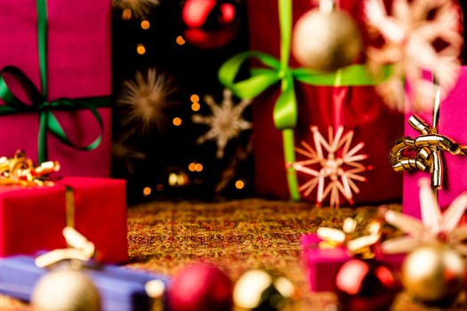 Christmas gifts, glitter balls and straw stars on a festive cloth. Seasonal background with focus on the golden bow tied around the magenta box on the right. Circular composition around a void center..