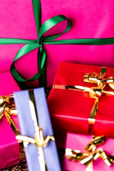 Close-up shot of a green bow tied around a magenta packet. Four smaller gift boxes with golden ribbons. All wrapped for any festive occasion..