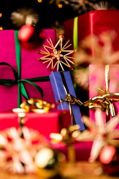 Unicolored Christmas gifts with bow knots. Shallow depth of field. Focus is on the golden bow around the blue box. Blurred shapes of baubles and straw stars in front and back..