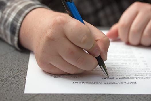 Closeup view of a hand of worker filling the form of employment agreement outdoors.