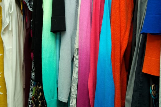 Close up of woman's clothing hanging in closet, showing various materials and colors