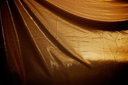 A dramatically draped and lit gold fabric background, filling frame.