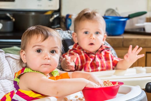 Two cute babies are eating breakfast together