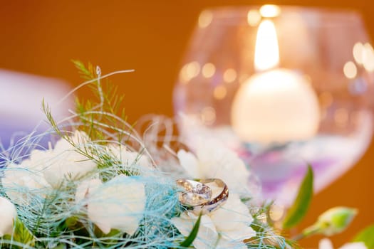 Wedding rings lying on white kytce a candle in a glass cup