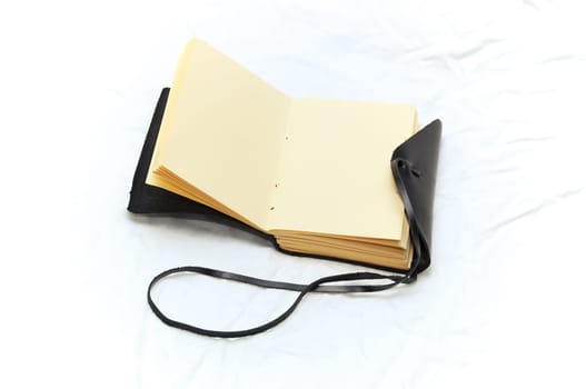 An old fashioned leather bound blank journal open to blank pages shot on white fabric.