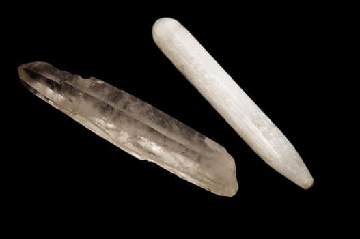 A quartz crystal wand and white selenite wand shot over black.