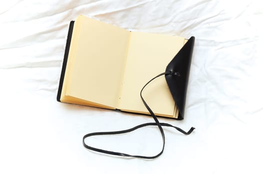 An old fashioned leather bound blank journal open to show blank pages shot over white fabric.
